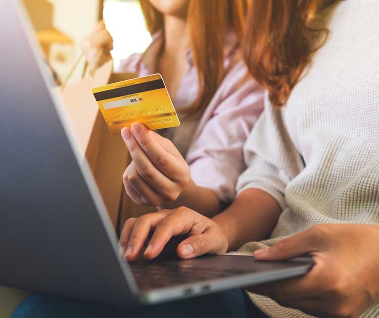 Photo of two persons viewing a laptop with one hand holding a credit card as in online shopping.