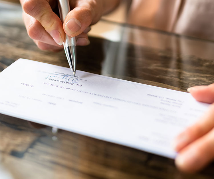 Close-up photo of hand with pen writing a check.