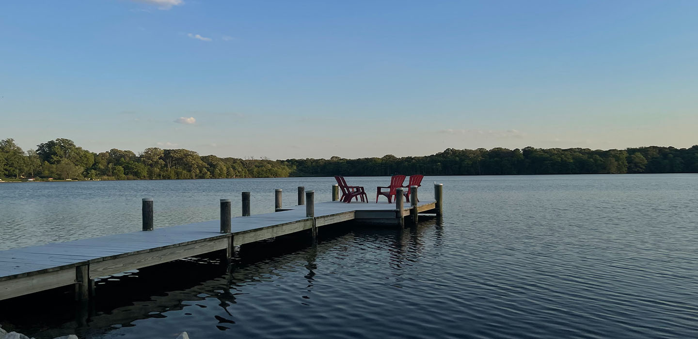 Beach chairs at the end of a pier deck on a lake.