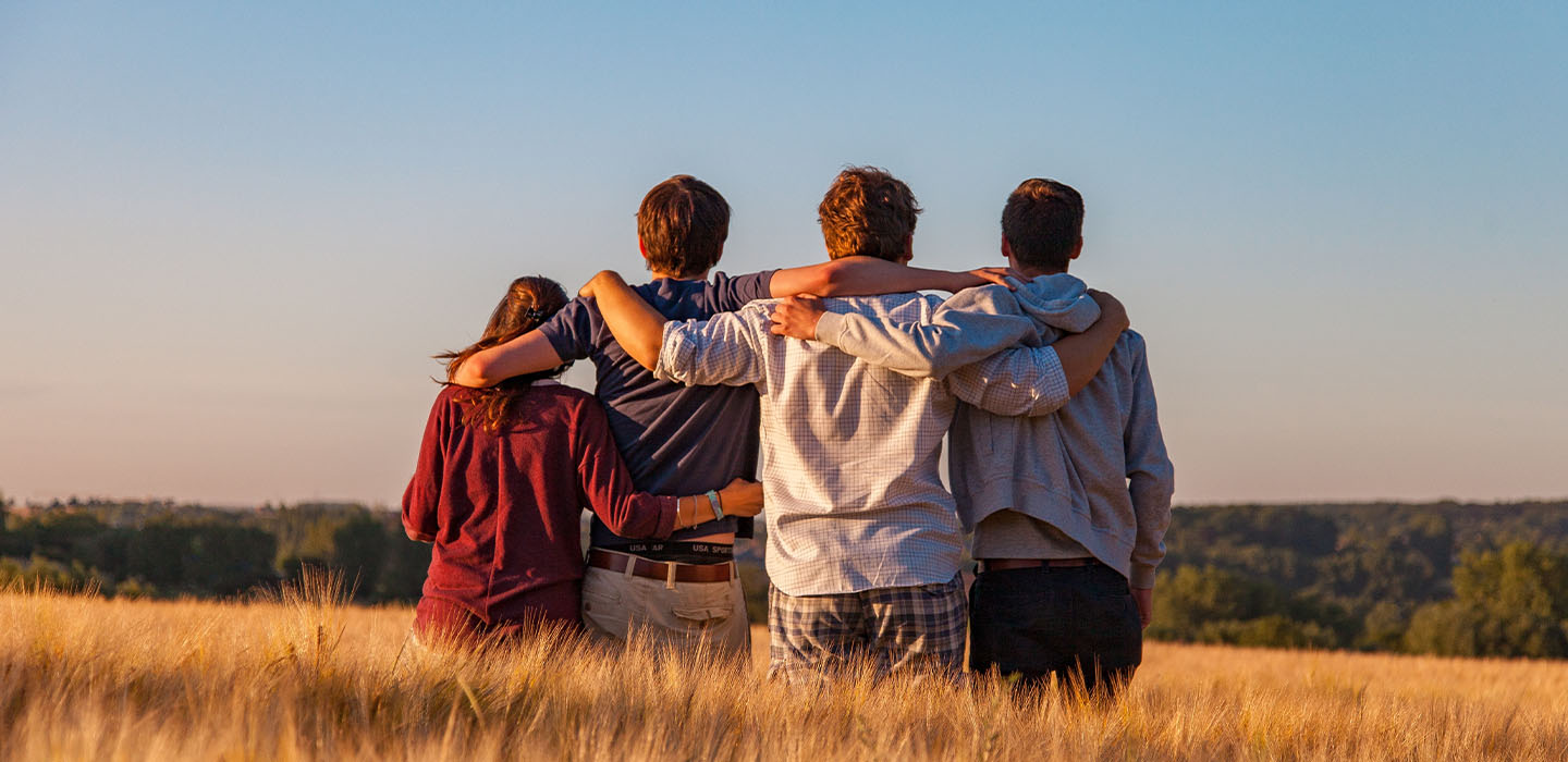 Four people with arms around waists looking away standing in a field.